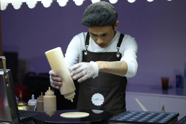 Chef expertly pouring dosa batter onto a hot tava in the bustling kitchen of sūrya rasoi.