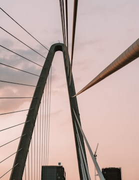 A towering cable-stayed bridge under construction with cranes and workers.