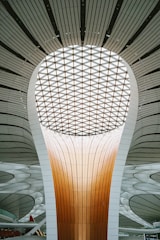 A futuristic architectural structure featuring a large, luminous dome with a patterned ceiling and a towering central column. The design incorporates smooth lines and a combination of warm and neutral tones, creating a sense of modernity and innovation.