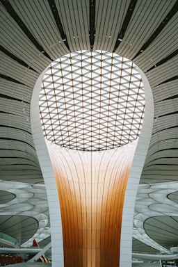 A futuristic architectural structure featuring a large, luminous dome with a patterned ceiling and a towering central column. The design incorporates smooth lines and a combination of warm and neutral tones, creating a sense of modernity and innovation.