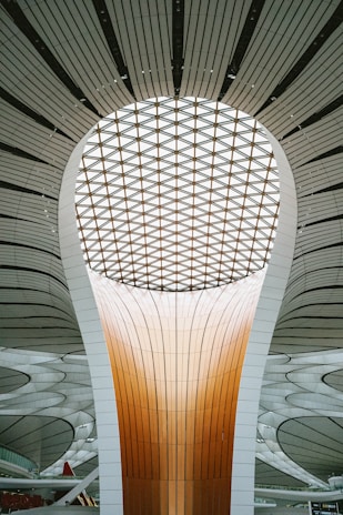 A futuristic architectural structure featuring a large, luminous dome with a patterned ceiling and a towering central column. The design incorporates smooth lines and a combination of warm and neutral tones, creating a sense of modernity and innovation.