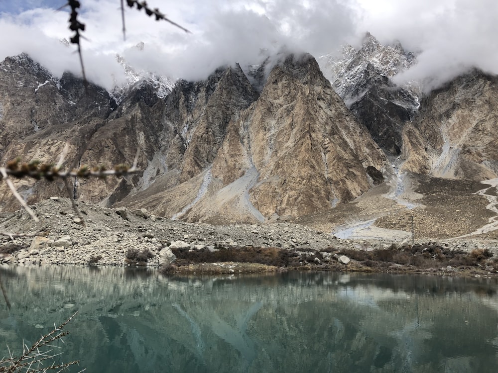 a lake surrounded by mountains under a cloudy sky