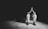 A person sitting alone on a chair in a dimly lit environment with their head bowed and hands pressed together, suggesting a moment of contemplation or prayer.