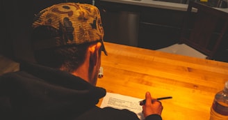 a man sitting at a table writing on a piece of paper