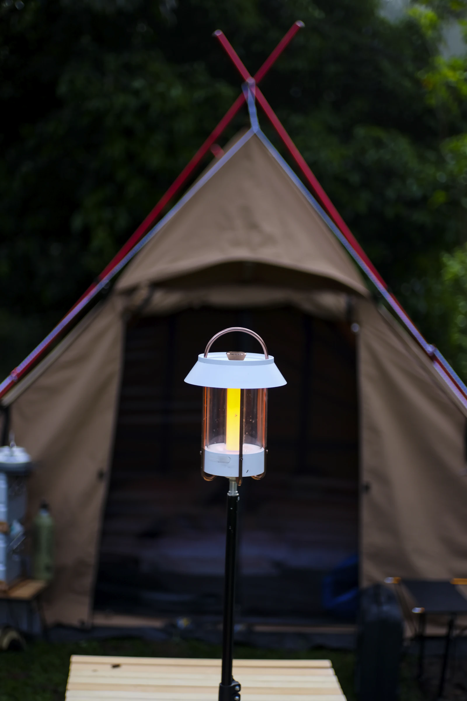 Camping lantern glowing on an outdoor table with tents in the background