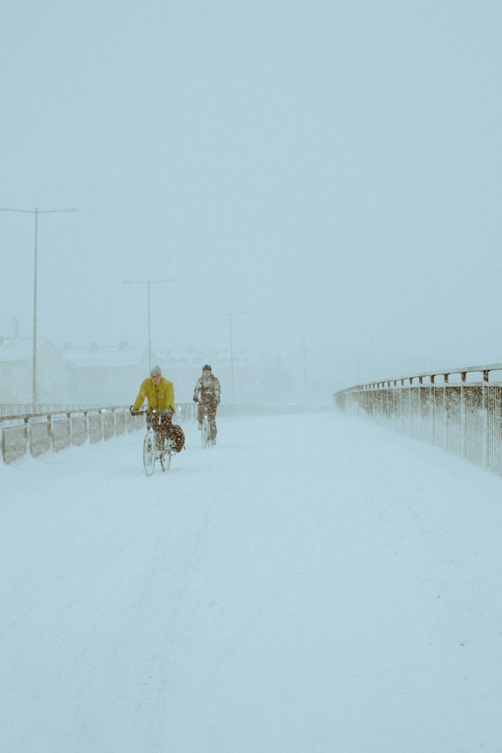 a couple of people riding bikes down a snow covered road