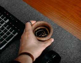 Close-up of hands typing on a keyboard with a cup of coffee nearby.