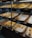 A display of freshly baked pastries is arranged in woven baskets on shelving units. The pastries have golden-brown, flaky crusts and are placed on white parchment paper. Price tags are visible, with various prices marked, indicating different types of pastries available.