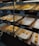 A display of freshly baked pastries is arranged in woven baskets on shelving units. The pastries have golden-brown, flaky crusts and are placed on white parchment paper. Price tags are visible, with various prices marked, indicating different types of pastries available.