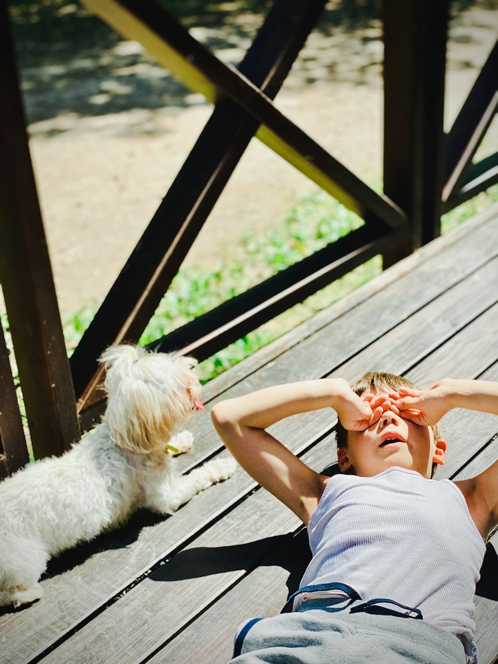 a man laying on a wooden deck next to a white dog