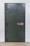 A large, heavy metal vault door set within a concrete or brick wall. The door features a circular combination lock and a metal handle bar. The surface has a slightly textured, industrial appearance.