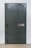 A large, heavy metal vault door set within a concrete or brick wall. The door features a circular combination lock and a metal handle bar. The surface has a slightly textured, industrial appearance.