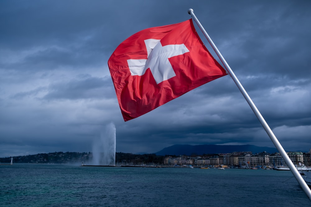 a swiss flag blowing in the wind near a body of water