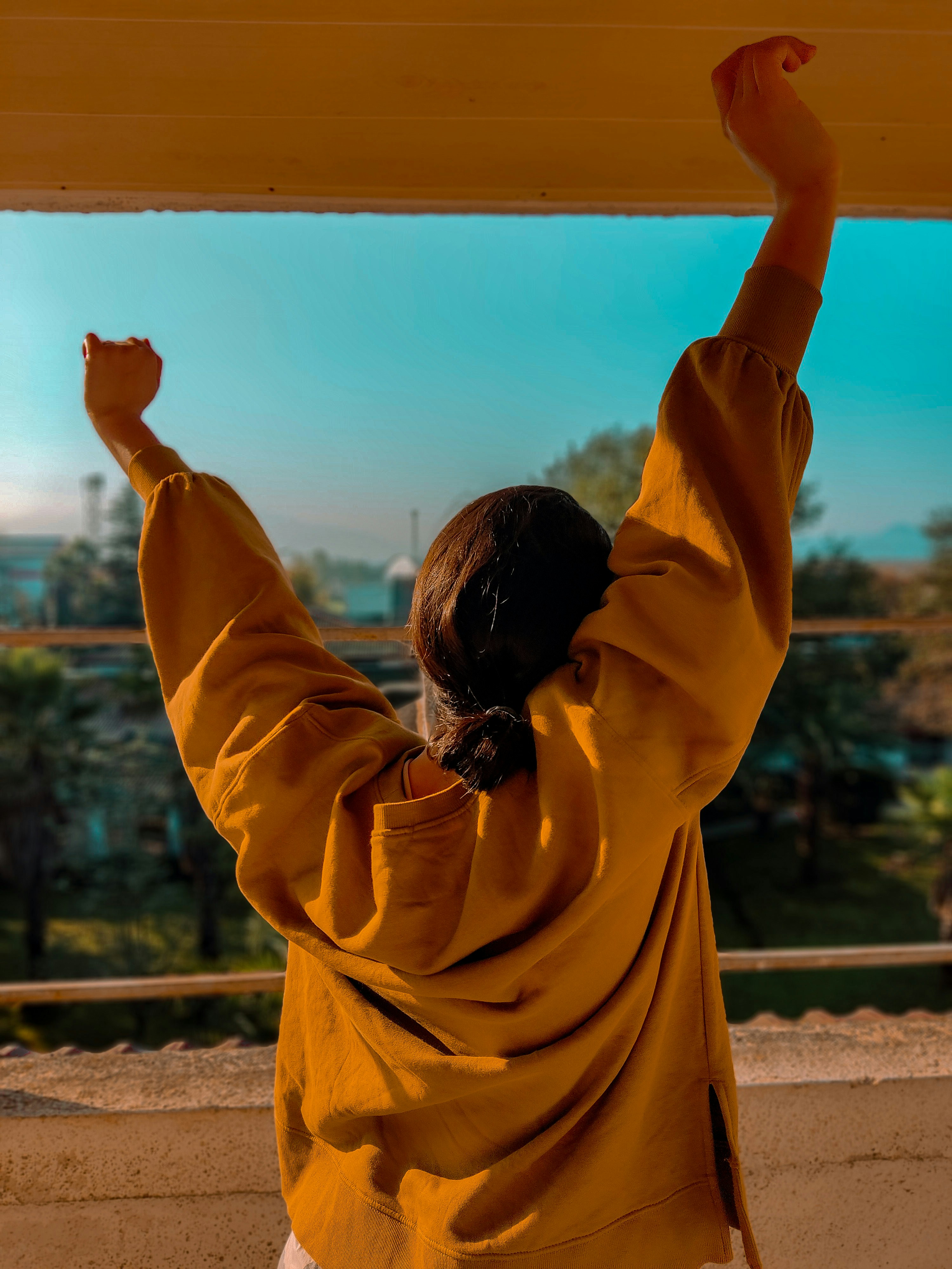 Seorang wanita berjaket kuning memegang papan selancar
