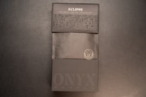 A dark themed packaging design for a product labeled 'Eclipse'. The packaging features embossed floral patterns and text. The phrase 'Bakers Chocolate' along with 'NYX Coffee' is visible, along with an illustration of a skull with a mustache.