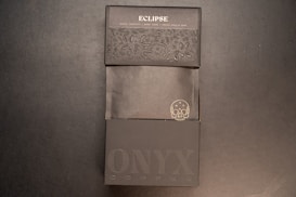 A dark themed packaging design for a product labeled 'Eclipse'. The packaging features embossed floral patterns and text. The phrase 'Bakers Chocolate' along with 'NYX Coffee' is visible, along with an illustration of a skull with a mustache.