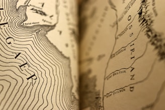 A detailed close-up of a sepia-toned map featuring contour lines and legible text, including geographic names such as Ossiriand and River Brilthor. The focus transitions smoothly from sharp details to a softer blur, emphasizing the intricacy of the cartographic design.