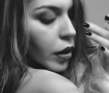 A black and white close-up portrait of a woman with her eyes closed, showcasing her facial features and textured hair. Her lips are slightly parted, and she appears to be in a contemplative or serene state.