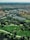 Aerial view of a cityscape blending urban and natural environments, featuring numerous residential buildings interspersed with lush green parks. The foreground includes well-maintained grassy areas and walking paths, leading to a densely built urban area in the background.