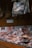 Various cuts of meat are vacuum-sealed in clear plastic packaging, displayed on a wooden counter. Above the counter, additional packaged fish and meats hang. The background consists of a wooden wall with decorative elements and muted lighting.
