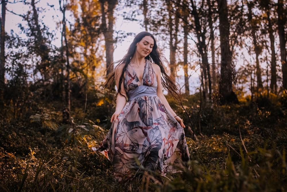 a woman in a dress walking through a forest