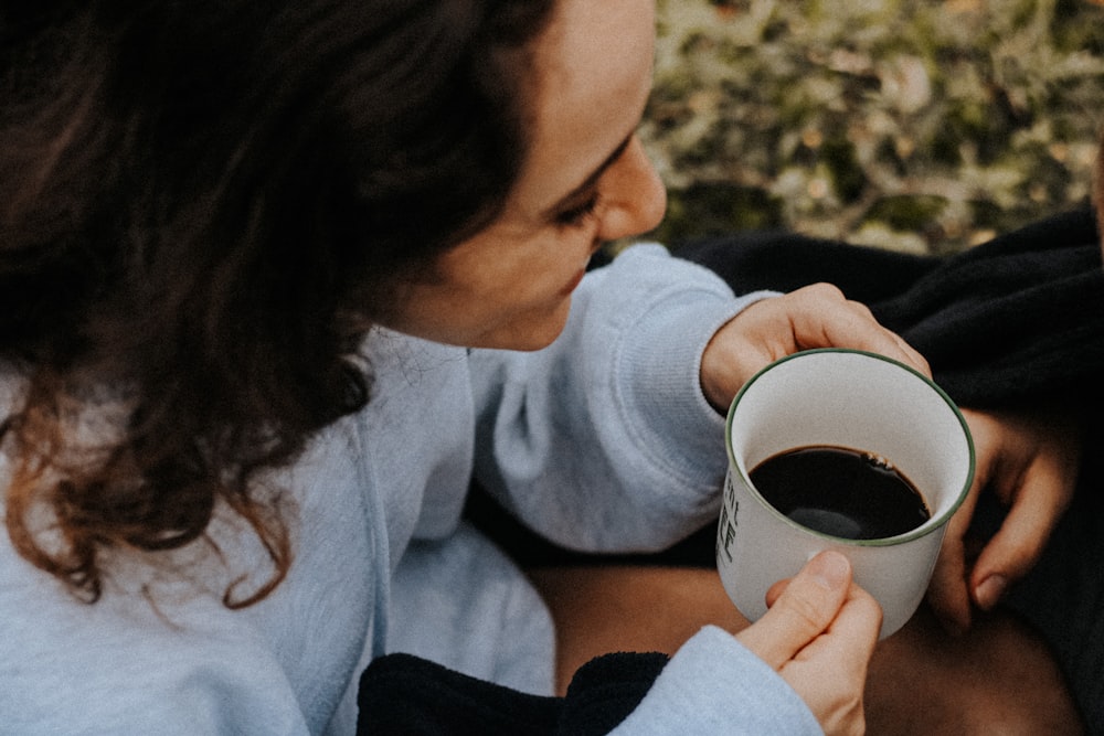 a woman holding a cup of coffee while sitting next to a man