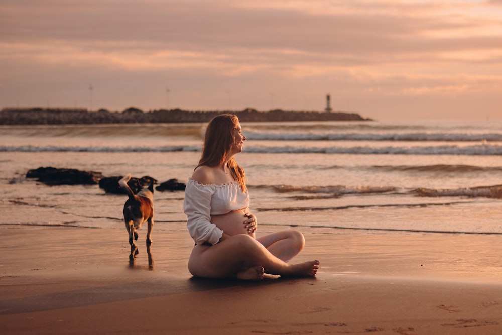 a woman sitting on a beach next to a dog