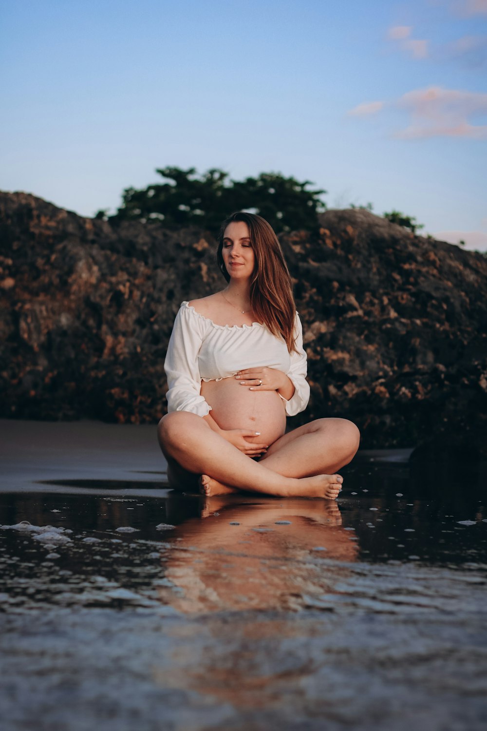 a pregnant woman sitting on a rock in the water