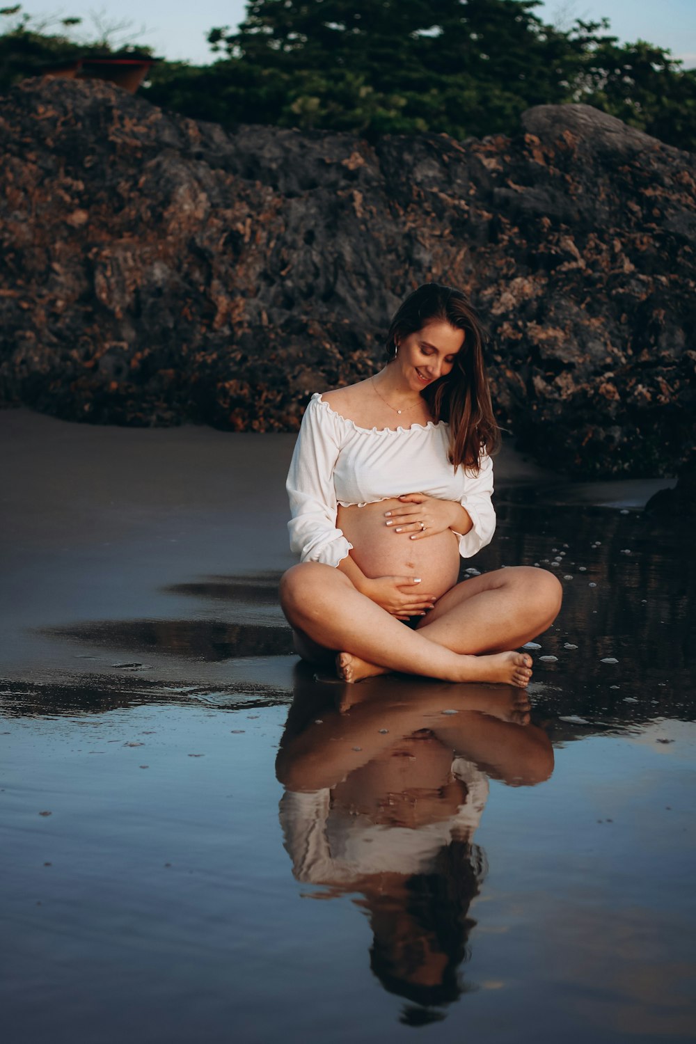 Eine schwangere Frau sitzt am Strand