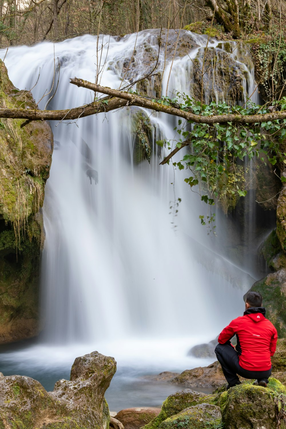 a man sitting on a rock looking at a waterfall