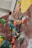 A person is bouldering on an indoor climbing wall with various colorful holds in different shapes and sizes. The climber is wearing casual clothes and climbing shoes, reaching for a hold above them.