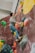 A person is bouldering on an indoor climbing wall with various colorful holds in different shapes and sizes. The climber is wearing casual clothes and climbing shoes, reaching for a hold above them.