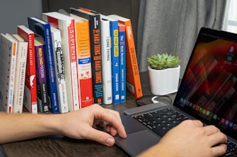 A focused student working on a laptop surrounded by notes and a green plant.