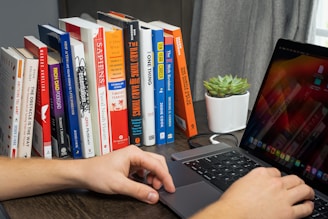 A student working intently on a laptop surrounded by technical books and notes.