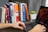 A happy student working on a laptop with books around.