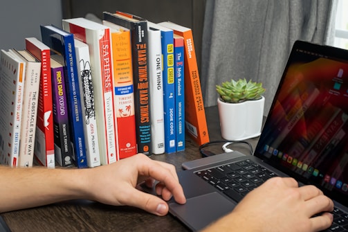 Photo of a person working on a laptop surrounded by digital books and notes.