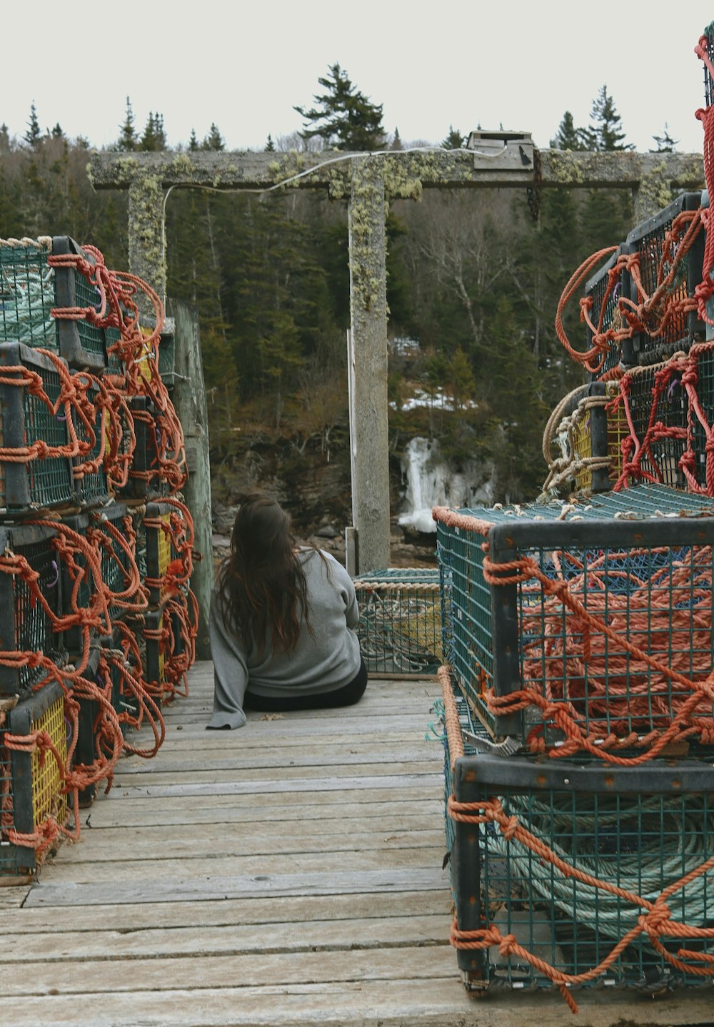 a woman sitting on a dock next to a pile of lobster traps
