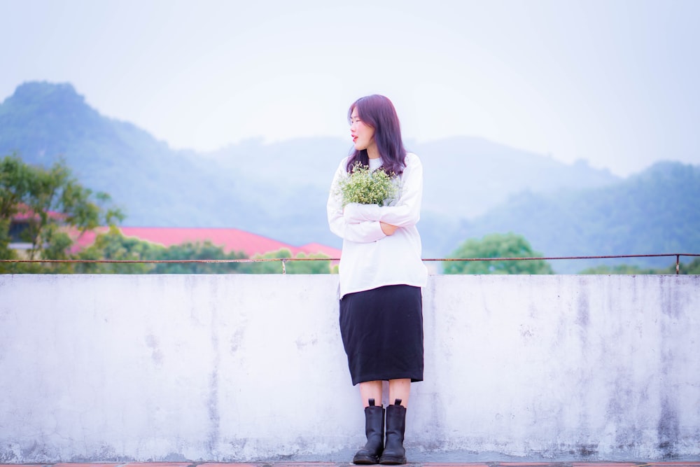 a woman holding a bunch of flowers standing next to a wall