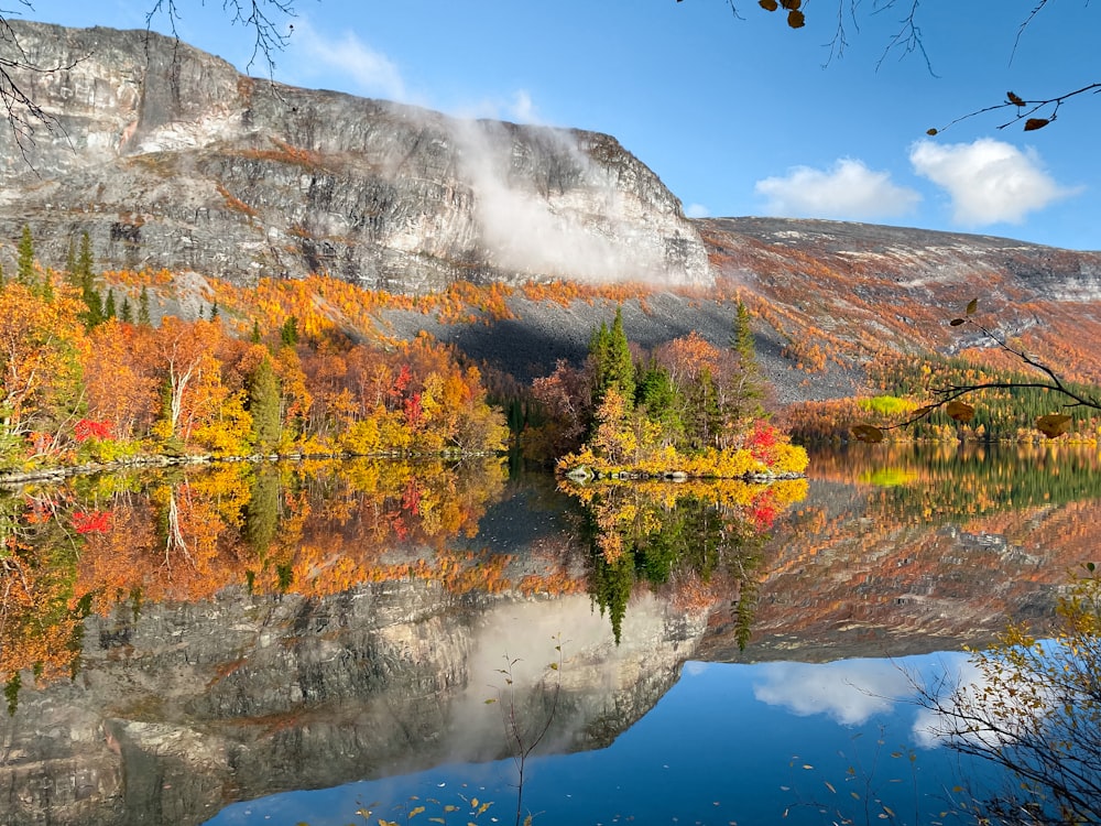 a lake surrounded by a mountain covered in fall foliage