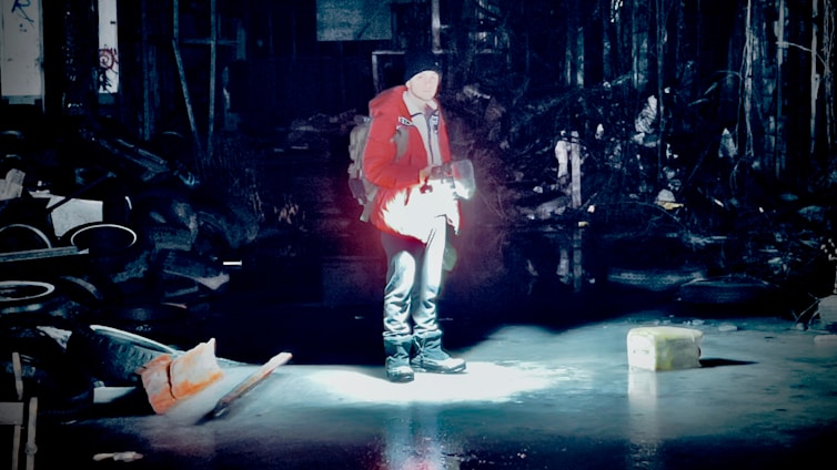 A safety inspector examining a light fixture with a flashlight in a dimly lit indoor space.
