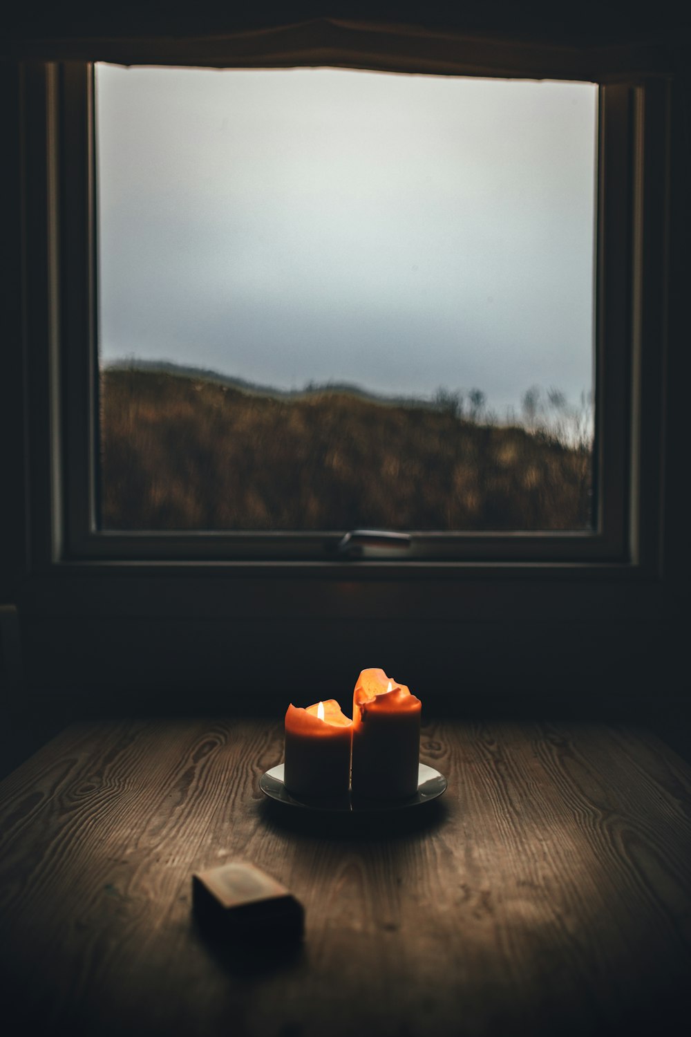Una vela sentada encima de una mesa de madera junto a una ventana