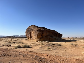 A weathered petroglyph carved into sunlit sandstone, surrounded by rugged desert terrain.