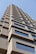 A tall building with a modern architectural design featuring textured concrete and large rectangular windows. The structure rises into a clear blue sky, capturing a perspective that emphasizes its height and geometric patterns.