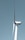 A large wind turbine stands tall against a clear blue sky, with three elongated blades extending from its hub. The turbine's tower is white and cylindrical, supporting the machinery at the top labeled with 'GE Wind Energy 15i'.