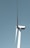A large wind turbine stands tall against a clear blue sky, with three elongated blades extending from its hub. The turbine's tower is white and cylindrical, supporting the machinery at the top labeled with 'GE Wind Energy 15i'.