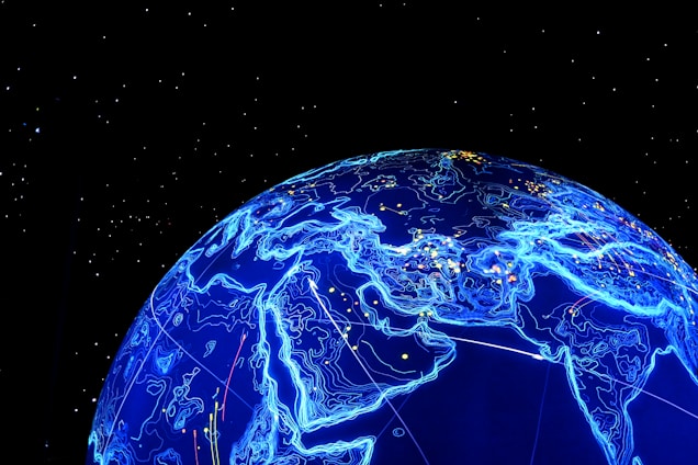 A glowing blue digital representation of the Earth is depicted, highlighting continents with illuminated contour lines against a black starry background. Small lights appear scattered across the surface, resembling cities or data points.