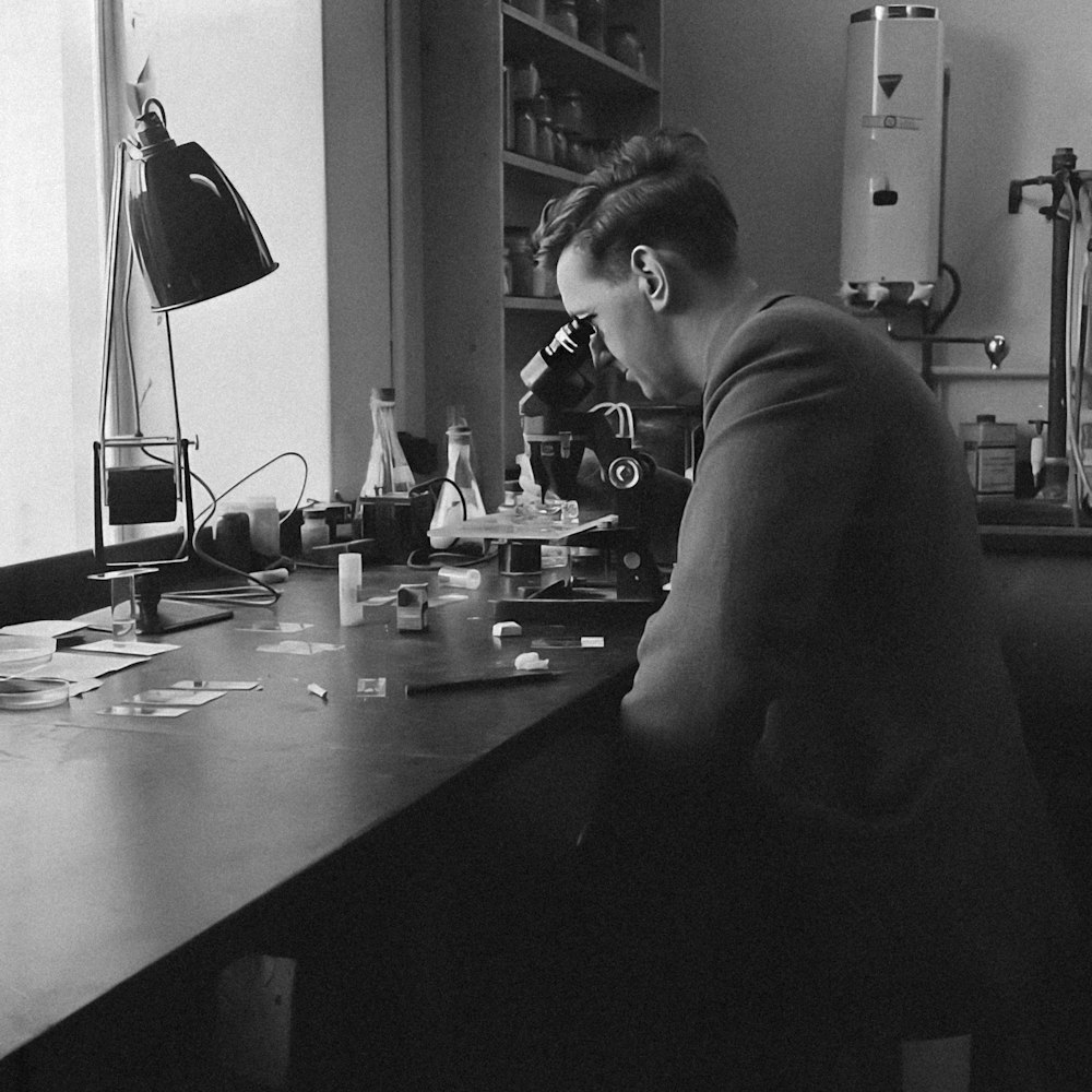a man sitting at a desk in front of a microscope