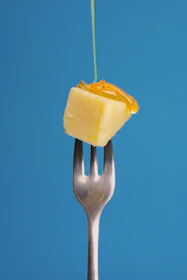 Close-up of a hand holding a delicate slice of cheese paired with a drizzle of honey, capturing the texture and richness.