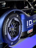 A close-up of a car's rear wheel featuring Bridgestone Potenza tires. The car has a sleek, modern design with a blue and black color scheme. The logo and branding for Volkswagen ID and Castrol are visible, suggesting it is a high-performance electric vehicle.