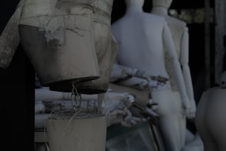 Several abstract mannequin parts are arranged in an artful, disorganized manner. The background is dark, casting shadows that give the scene a slightly eerie and mysterious atmosphere. The mannequins are predominantly white and cream-colored, with some showing signs of wear and tear, such as scratches and peeling paint.